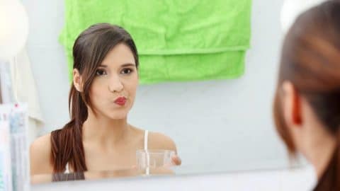 Young woman using a zinc-activated mouthwash for dry mouth, standing in a bathroom and swishing the liquid for oral hydration and freshness.